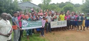 Familien aus dem Vanille-Dorf halten neue Schulhefte hoch, davor Banner mit „Danke schön! Misaotra betsaka!“