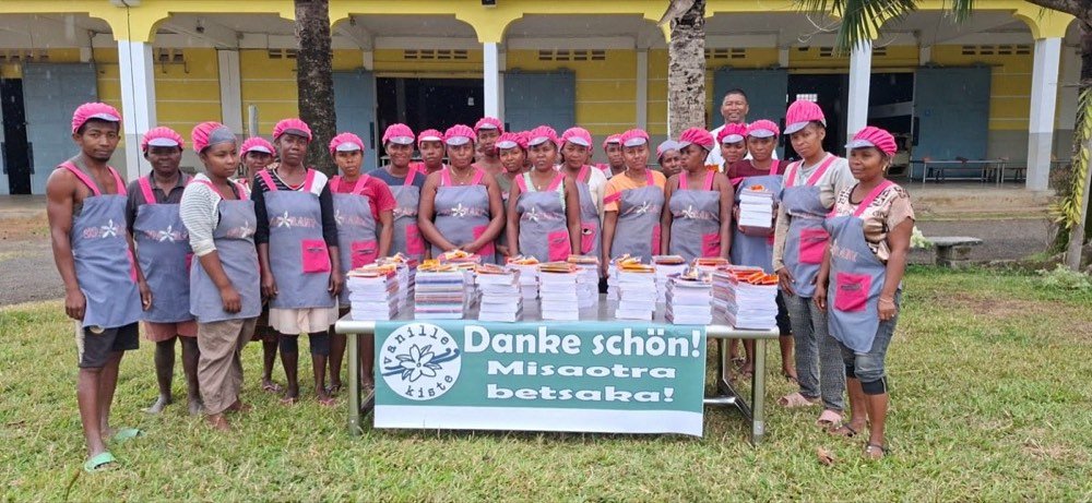Das Team vor Ort in Madagaskar mit Stapeln von Schulheften und dem Vanillekiste-Banner